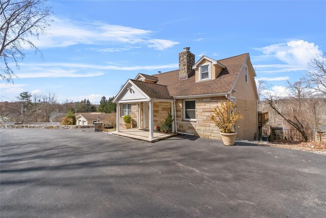 view of front of home with a chimney, a shingled roof, and stone siding