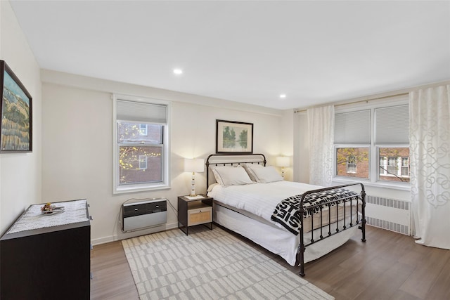 bedroom with radiator, light wood-style floors, multiple windows, and heating unit
