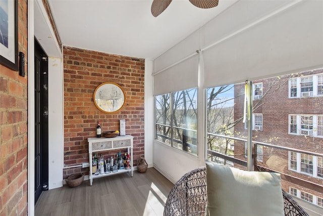 sunroom with brick wall, ceiling fan, and wood finished floors