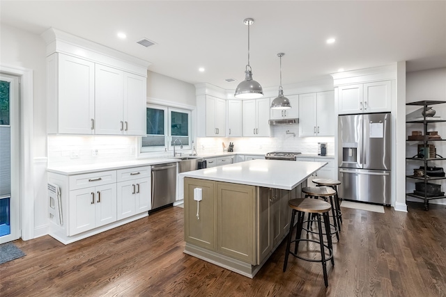 kitchen featuring dark wood-style flooring, stainless steel appliances, a center island, under cabinet range hood, and visible vents