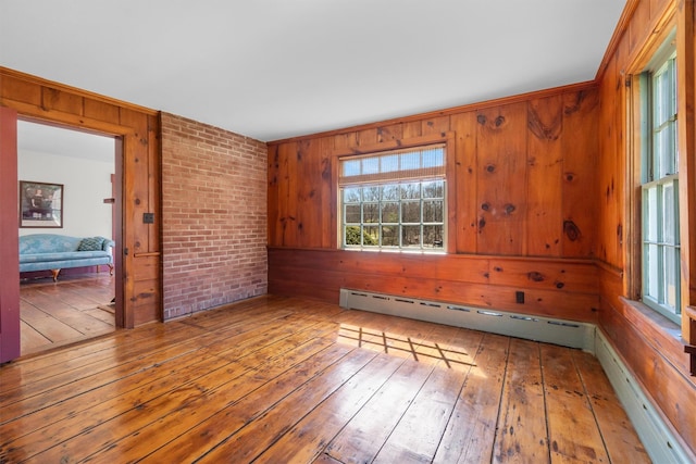 empty room with a baseboard heating unit, wooden walls, and hardwood / wood-style flooring