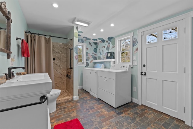 full bath with tiled shower, two vanities, baseboards, and washer and clothes dryer