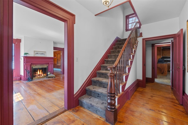 stairs with wood-type flooring and a glass covered fireplace