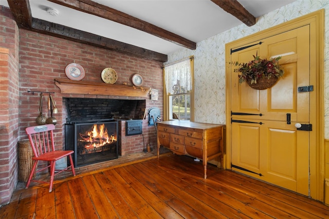 interior space with wallpapered walls, beam ceiling, a brick fireplace, and hardwood / wood-style flooring