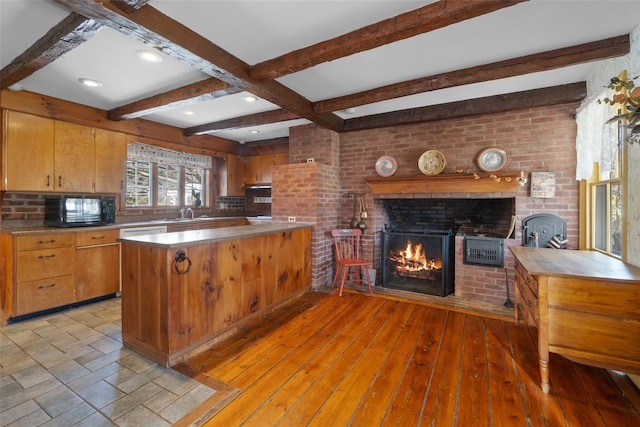 kitchen featuring beamed ceiling, a fireplace, black microwave, a peninsula, and light wood-type flooring