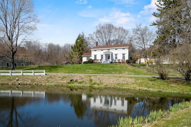 back of house with a water view, a yard, and a chimney