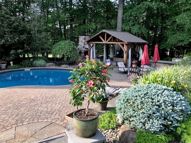 outdoor pool with a gazebo, a patio area, and view of wooded area