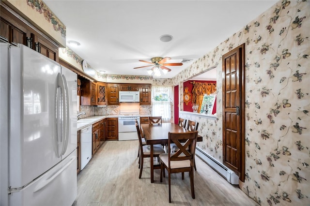 kitchen with a sink, a baseboard radiator, wallpapered walls, and white appliances