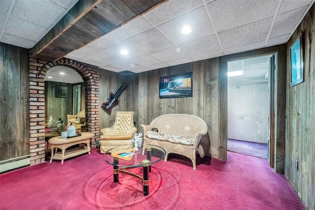 living area featuring a drop ceiling, carpet, wood walls, and a baseboard heating unit
