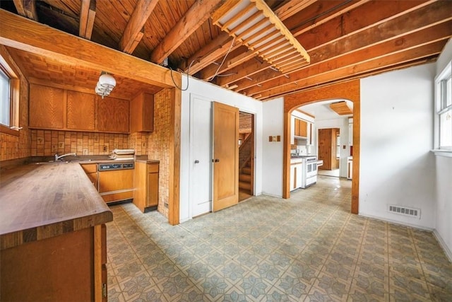 kitchen featuring arched walkways, brown cabinetry, paneled dishwasher, high end range, and visible vents