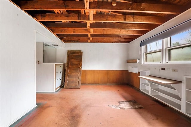 interior space featuring wood walls, unfinished concrete flooring, and a wainscoted wall
