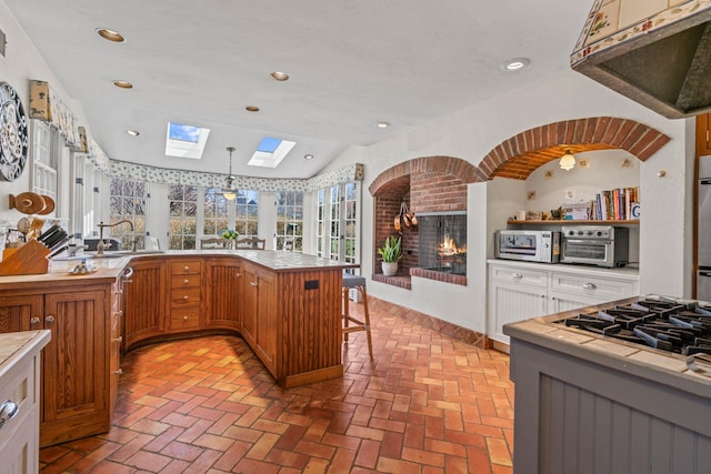 3 Wincoma Dr, Huntington Bay, NY 11743 - kitchen featuring a brick fireplace, recessed lighting, brick floor, a sink, and brown cabinetry