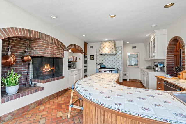 3 Wincoma Dr, Huntington Bay, NY 11743 - kitchen with a fireplace, glass insert cabinets, white cabinetry, tile countertops, and radiator