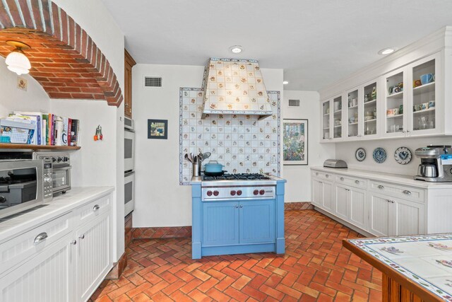 3 Wincoma Dr, Huntington Bay, NY 11743 - kitchen featuring custom range hood, brick floor, visible vents, white cabinets, and appliances with stainless steel finishes