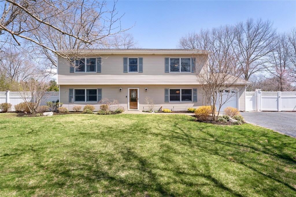colonial home featuring driveway, a front yard, fence, and a garage