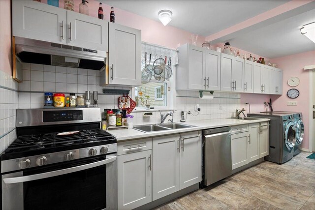 kitchen featuring light countertops, washer and clothes dryer, under cabinet range hood, decorative backsplash, and appliances with stainless steel finishes