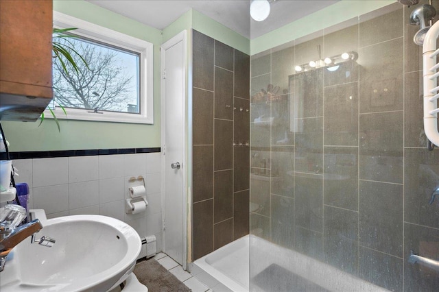 bathroom with a sink, a shower stall, a baseboard radiator, tile patterned flooring, and tile walls