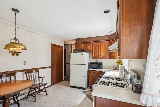 kitchen with a sink, light countertops, white appliances, under cabinet range hood, and brown cabinets