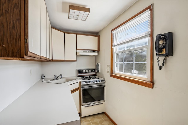 kitchen featuring white range with gas cooktop, light countertops, white cabinetry, under cabinet range hood, and a sink