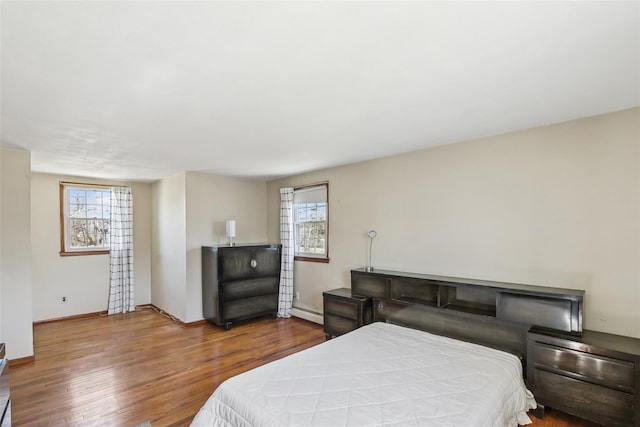 bedroom with a baseboard radiator, multiple windows, baseboards, and wood finished floors