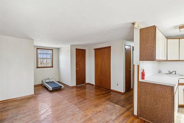 kitchen with a sink, light countertops, light wood finished floors, and baseboards