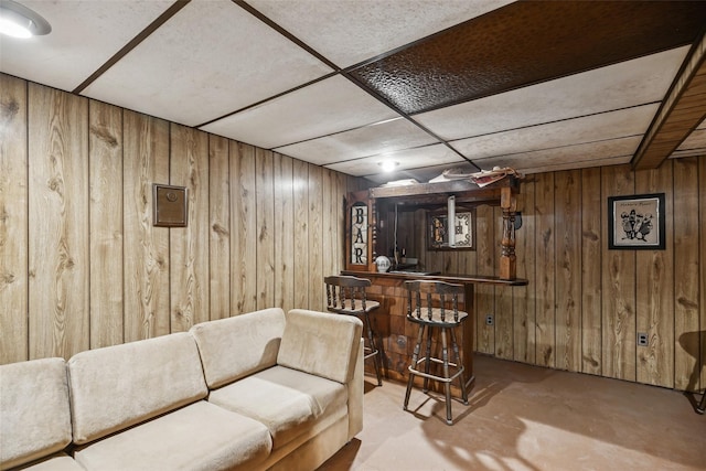bar with a paneled ceiling, a dry bar, wooden walls, and unfinished concrete flooring