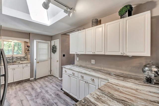 kitchen with light wood-type flooring, white cabinets, a skylight, light stone counters, and a sink