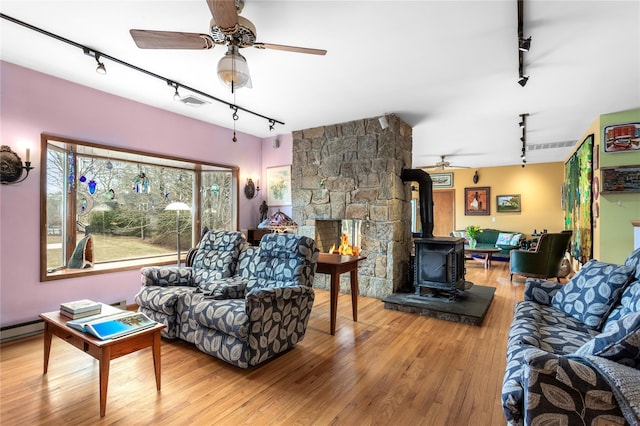 living area with track lighting, ceiling fan, a wood stove, and wood finished floors
