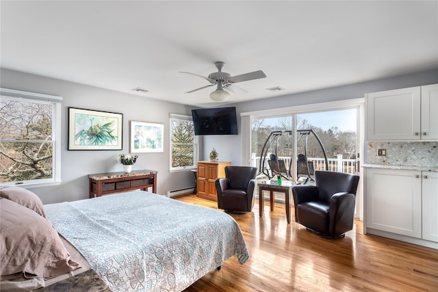 bedroom featuring a baseboard radiator, multiple windows, light wood-style flooring, and access to exterior
