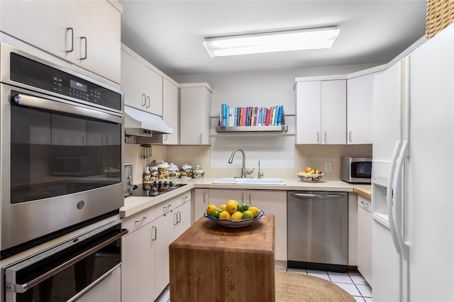 kitchen with stainless steel appliances, a sink, under cabinet range hood, light countertops, and white cabinetry