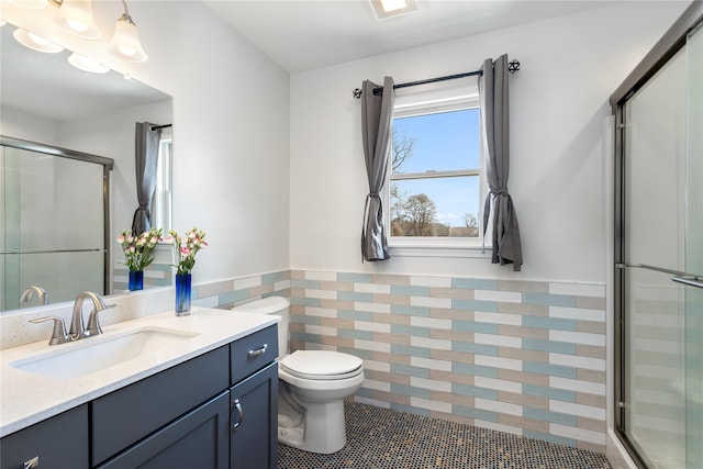 full bath with a wainscoted wall, tile patterned flooring, a stall shower, toilet, and vanity