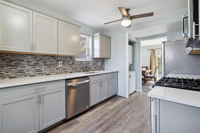 kitchen with a sink, decorative backsplash, a ceiling fan, stacked washer / drying machine, and appliances with stainless steel finishes