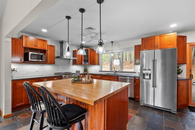 kitchen with wall chimney range hood, wooden counters, visible vents, stainless steel appliances, and a sink