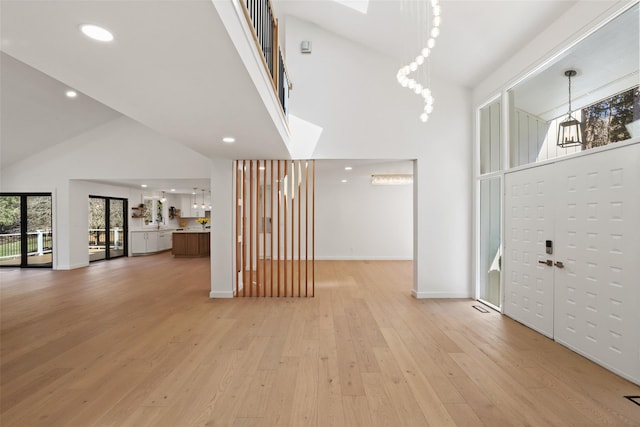 foyer entrance with high vaulted ceiling, recessed lighting, light wood-type flooring, and baseboards