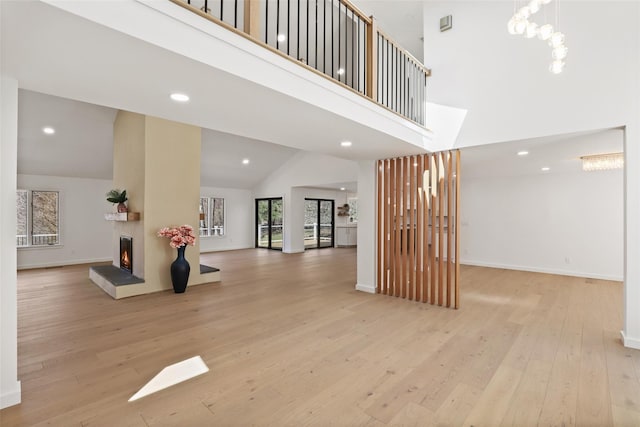 interior space with baseboards, high vaulted ceiling, wood-type flooring, and a warm lit fireplace