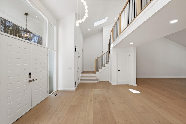 foyer entrance with a towering ceiling, baseboards, stairway, a skylight, and wood-type flooring