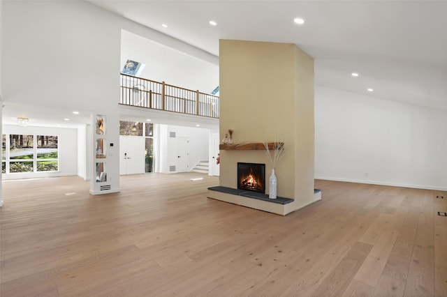 unfurnished living room with recessed lighting, a towering ceiling, a warm lit fireplace, and light wood-style flooring