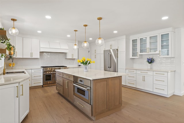 kitchen with custom exhaust hood, high quality appliances, white cabinetry, backsplash, and a sink