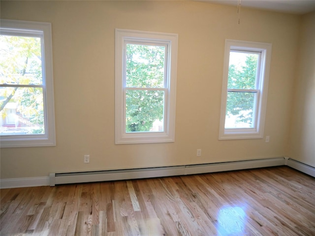 empty room with wood finished floors, a baseboard heating unit, and a wealth of natural light