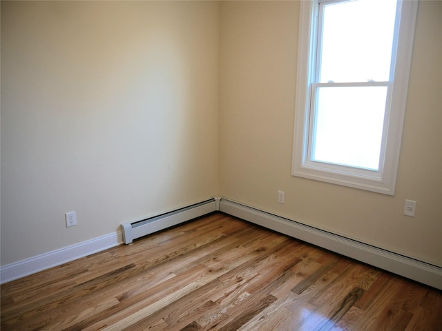 spare room featuring wood finished floors, a baseboard heating unit, and baseboards
