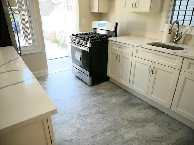 kitchen with light stone countertops, white cabinetry, a sink, and gas stove