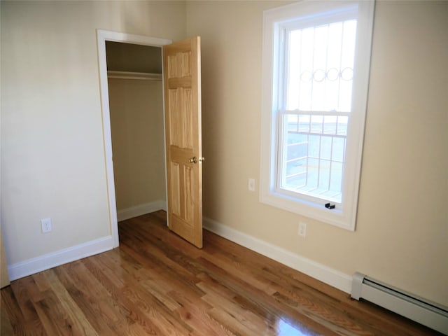 unfurnished bedroom featuring a closet, baseboards, a baseboard heating unit, and wood finished floors
