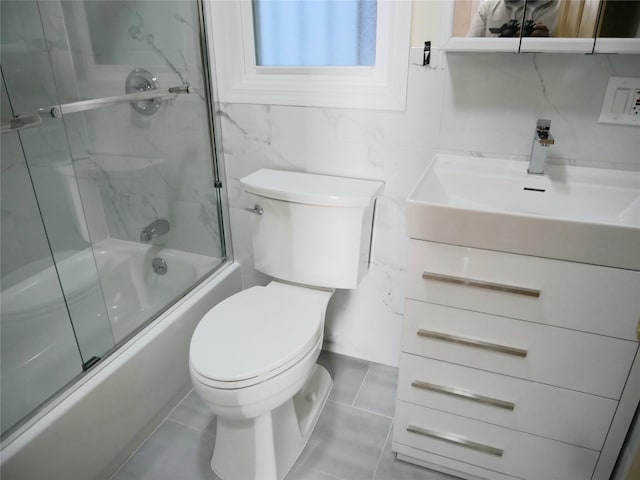 full bathroom with tile walls, toilet, vanity, and bath / shower combo with glass door