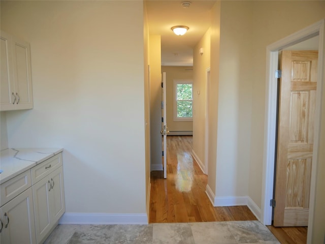 corridor featuring light wood-style flooring, baseboards, and baseboard heating