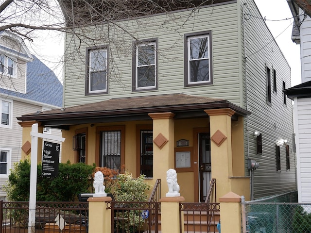view of front facade featuring a shingled roof, a fenced front yard, stucco siding, and covered porch