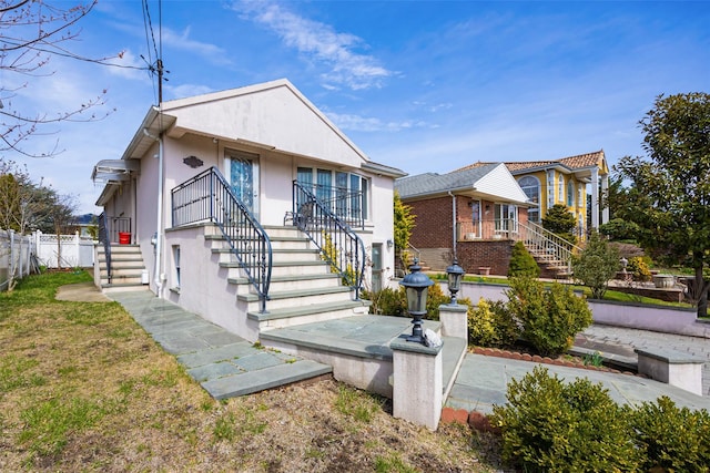 view of front of property featuring a front yard, stucco siding, fence, and stairs