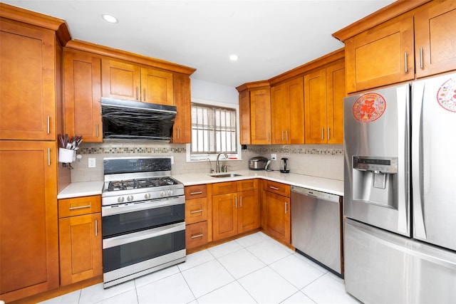 kitchen featuring light countertops, range hood, appliances with stainless steel finishes, a sink, and brown cabinetry