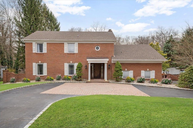 colonial inspired home with driveway, brick siding, a chimney, and a front lawn