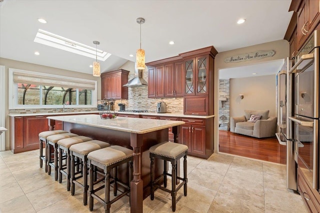 kitchen with wall chimney range hood, decorative backsplash, a kitchen bar, and a kitchen island