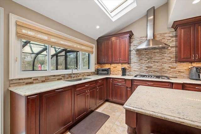 kitchen featuring stainless steel gas cooktop, a sink, wall chimney exhaust hood, tasteful backsplash, and lofted ceiling with skylight